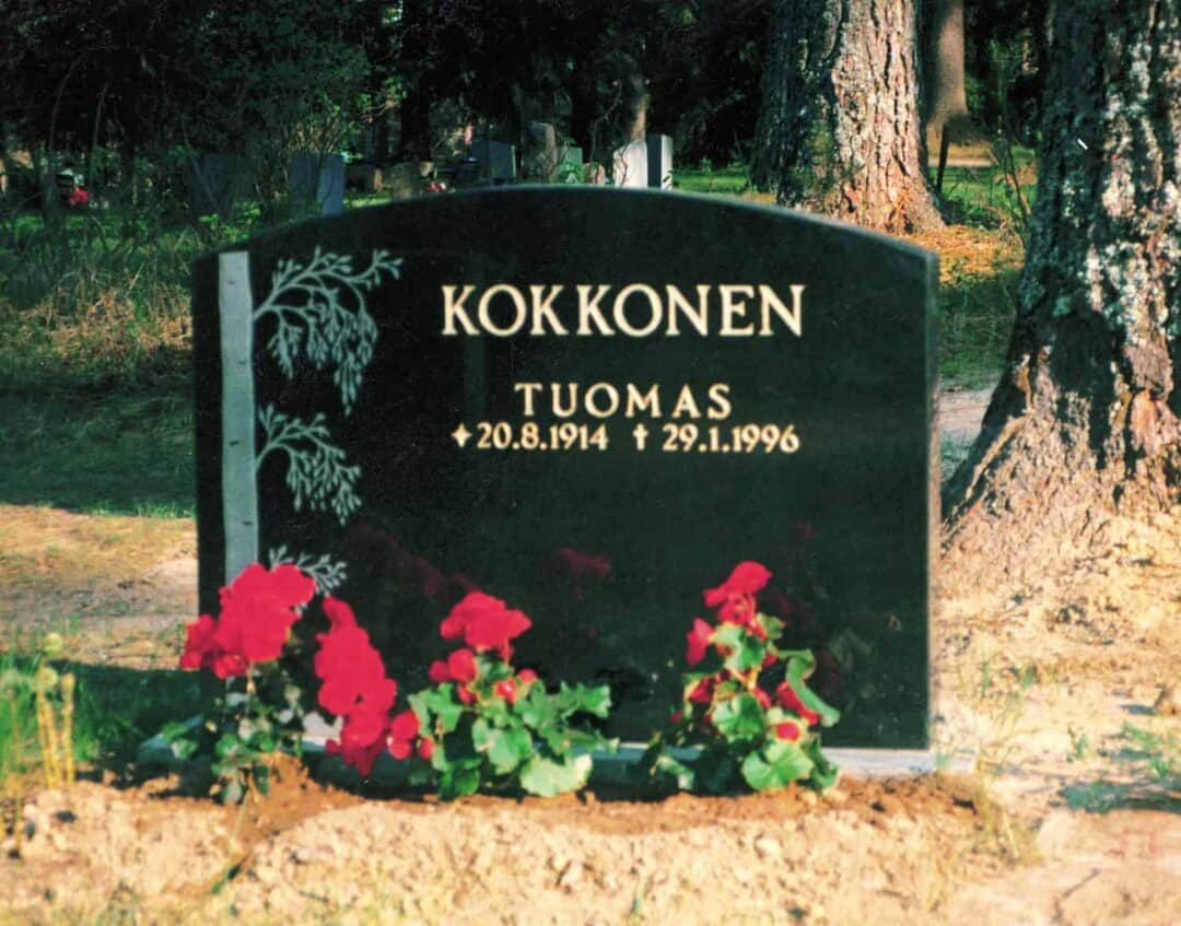 Kuvassa on hautakivi Kokkonen on yläosasta kaareva ja sen vasemmassa reunassa on puu.